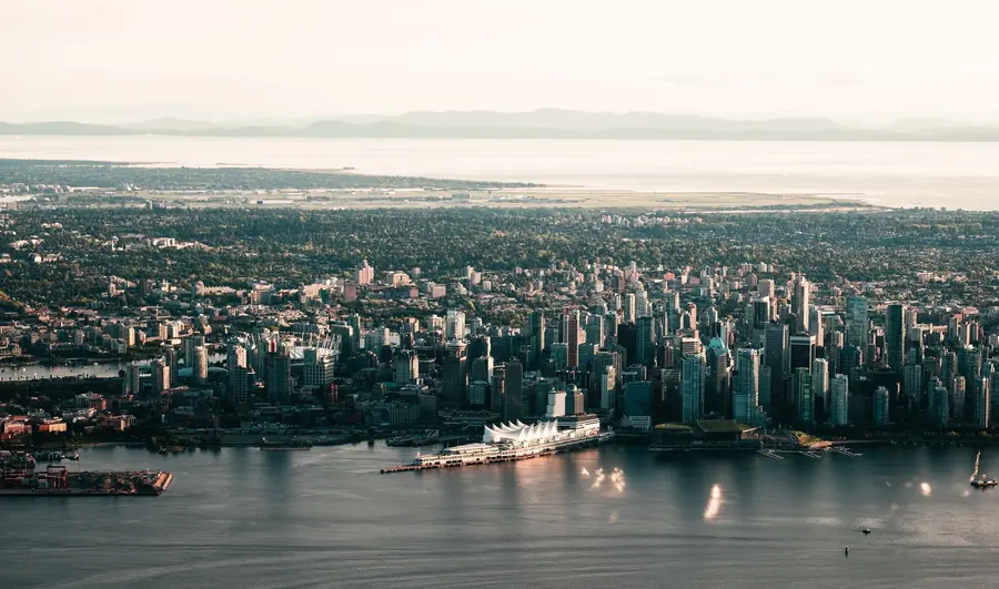 Aerial view of downtown Vancouver's towers and the white sails of the convention centre on the harbour, with the North Shore mountains behind