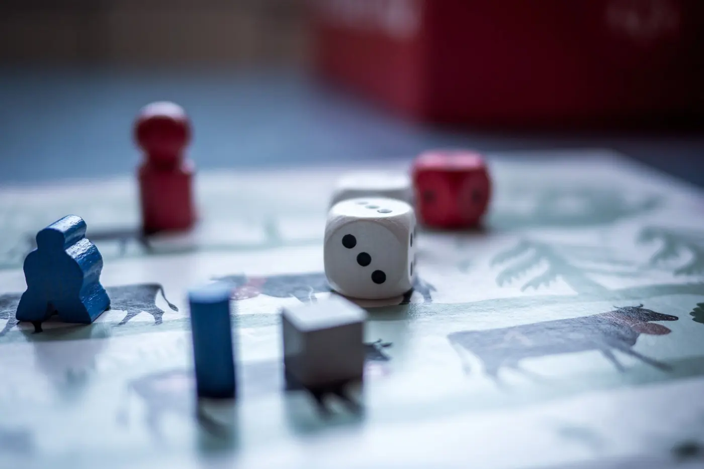 Wooden board-game pieces and a white die on a printed game board, photographed close up with a shallow depth of field