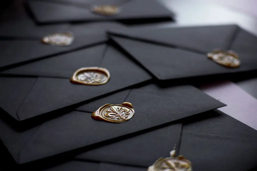 Black envelopes stacked at an angle, each closed with a gold wax seal pressed with a fleur-de-lis